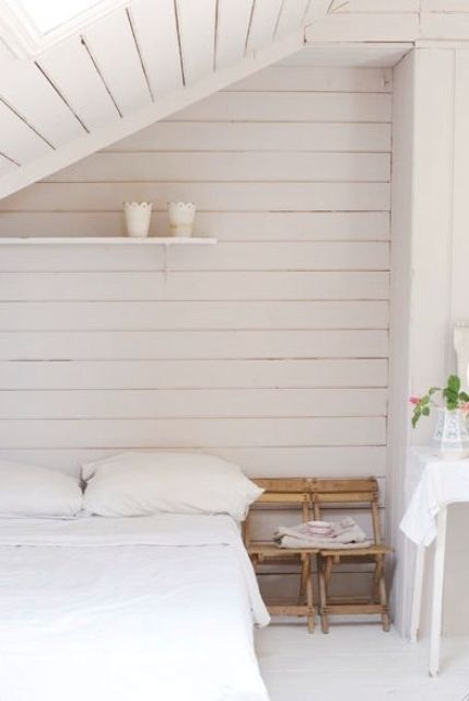 a small neutral bedroom with whitewashed walls and a ceiling, a simple bed and chairs and all neutral linens