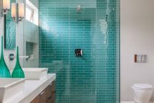 a stylish and bright bathroom with neutral tiles, tuquoise ones in the shower, a wooden vanity with a stone countertop and turquoise bottles