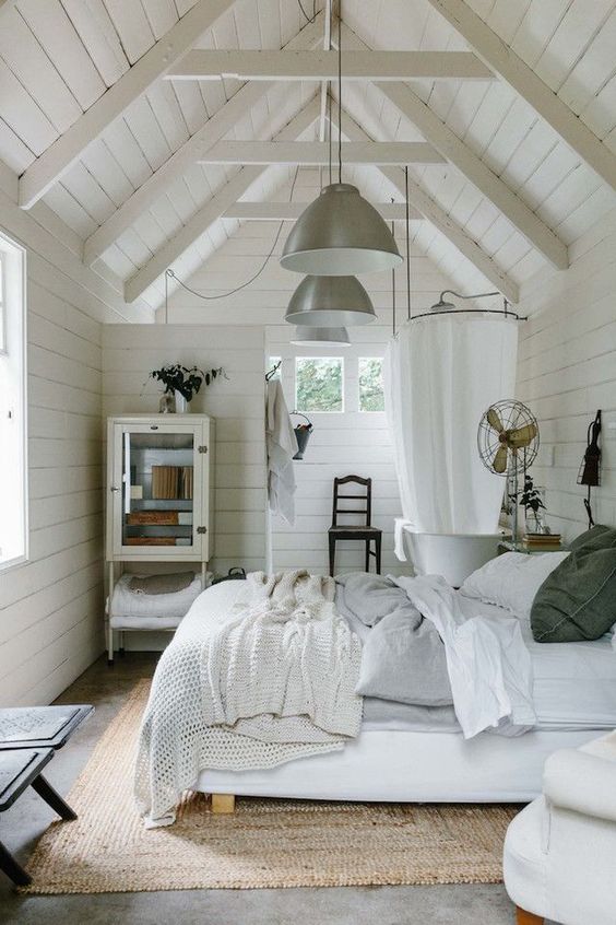 a vintage farmhouse bedroom with a bathroom with whitewashed wooden walls, vintage furniture and lamps and cozy bedding