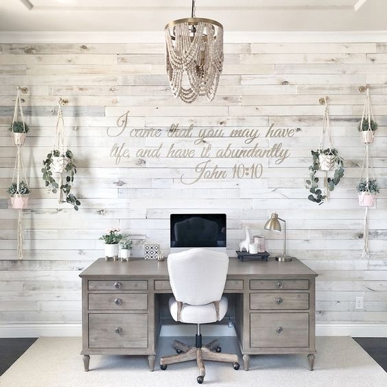 a vintage farmhouse home office with a whitewashed wooden wall, rustic furniture, a beaded chandelier and potted greenery