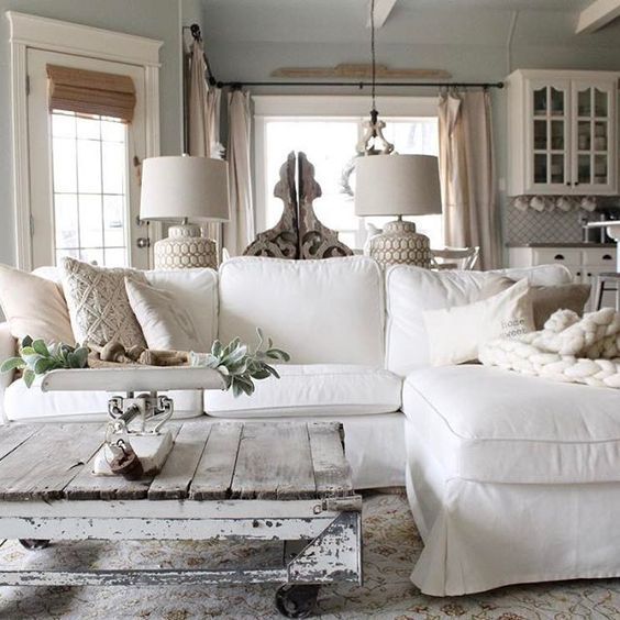 a vintage farmhouse living room with a white sectional, a whitewashed and distressed pallet coffee table, cool lamps and some greenery