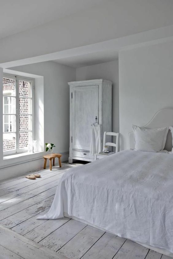 A vintage inspired bedroom with white walls, a whitewashed floor and whitewashed furniture plus lots of natural light