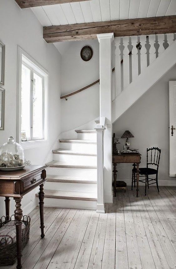 A vintage inspired entryway in white, with a whitewashed floor, wooden beams and vintage furniture
