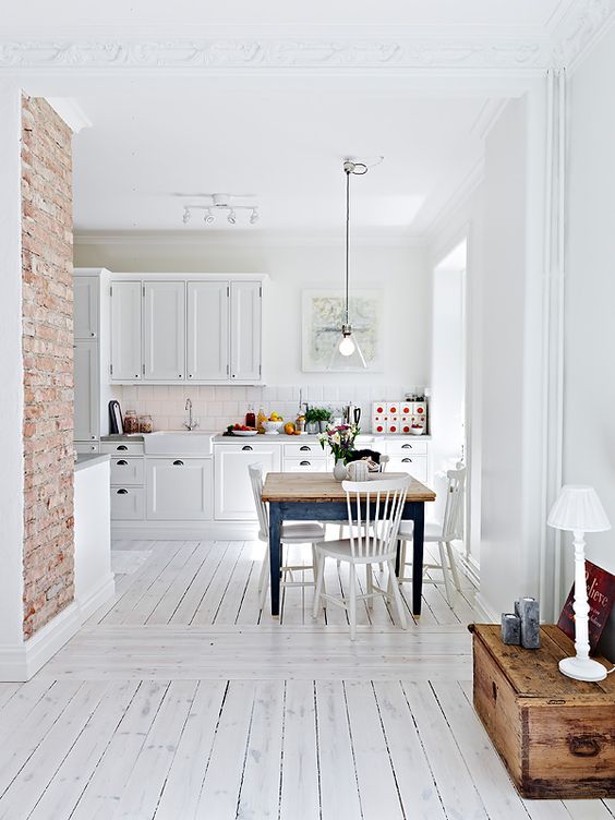 A vintage inspired kitchen with white walls, a whitewashed floor, white cabinets and a blue dining table