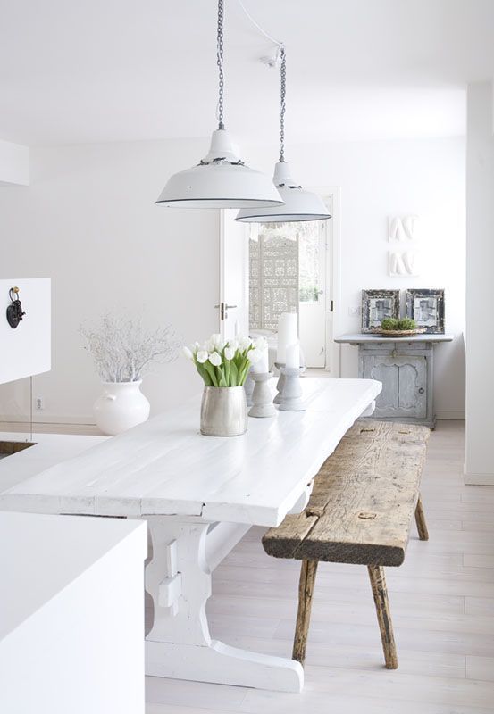 A vintage inspired white kitchen with white walls and a whitewashed floor, white and stained furniture plus greenery