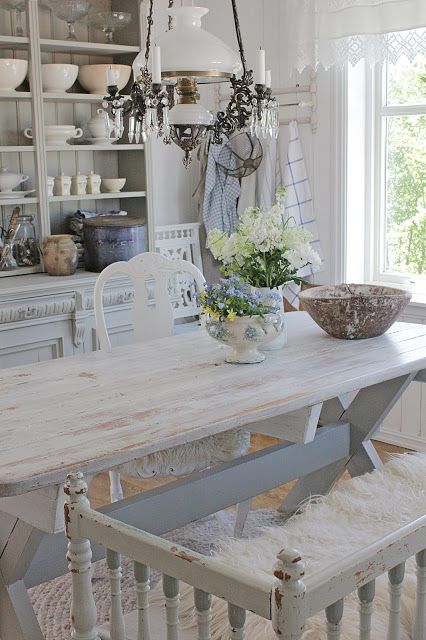 a vintage shabby dining space with a whitewashed table and chairs and a bench, a whitewashed buffet and some touches of blue
