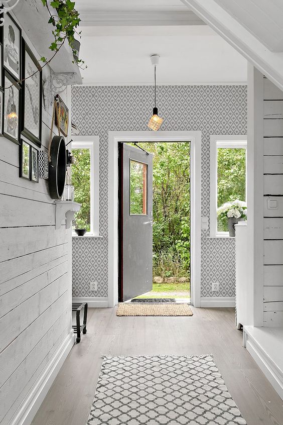 a welcoming Nordic entryway with wallpaper walls, a whitewashed floor and potted blooms plus a pendant lamp