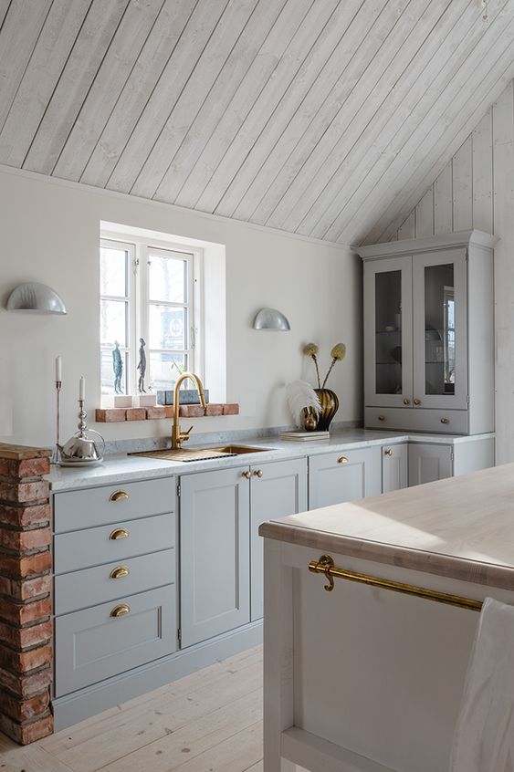 a welcoming neutral kitchen with whitewashed wooden walls and a ceiling, grey cabinets, a white kitchen island and touches of gold