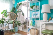 a welcoming tropical-inspired room with a turquoise accent wall, white and green furniture, a mirror table and a papasan chair plus lots of plants