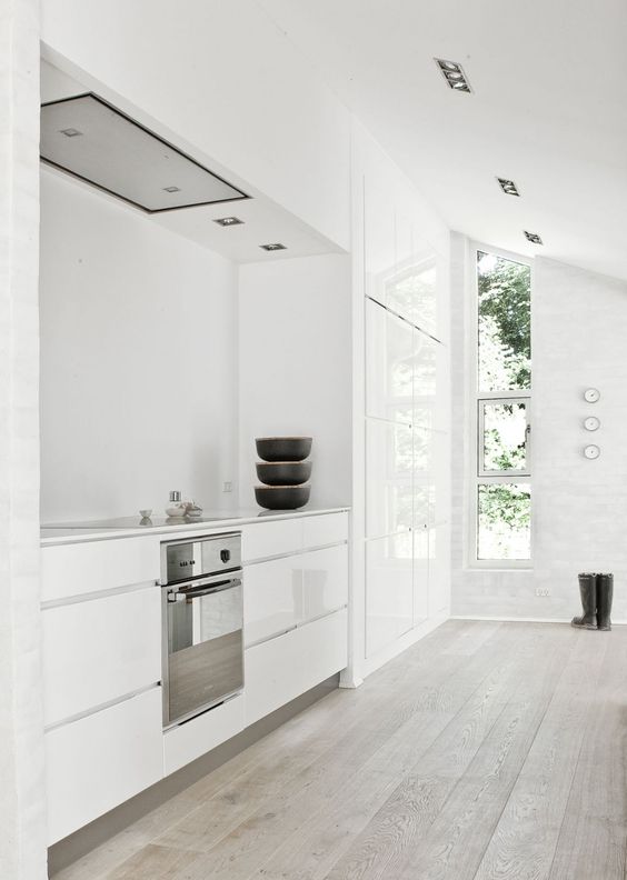 a white minimalist kitchen with a whitewashed floor, sleek cabinets and lots of natural light flooding the space