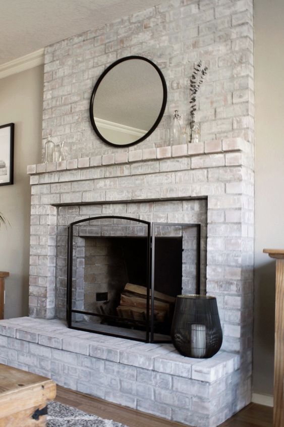 a whitewashed brick fireplace with a brick mantel, a round mirror, a metal frame and a candle lantern is stylish