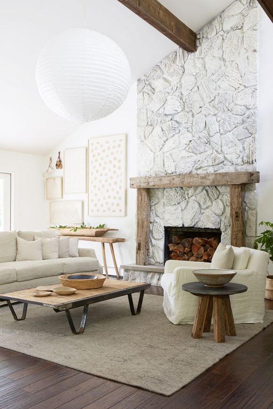 a whitewashed stone fireplace with a rough wood mantel, firewood inside brings a cozy farmhouse feel to the room