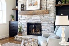 a whitewashed stone fireplace with a rough wooden mantel, vintage decor and a potted plant brings a farmhouse feel