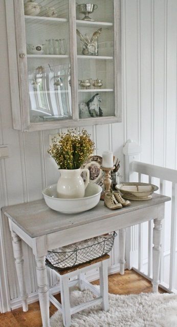 a whitewashed storage cabinet with a glass door and matching furniture items for a small and cozy shabby chic nook