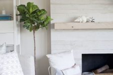 a whitewashed wood fireplace with a neutral mantel, firewood, a basket with pillows looks ethereal and chic