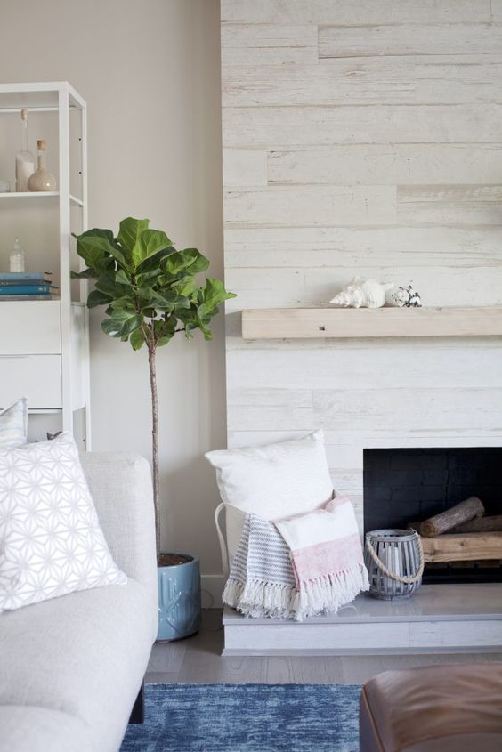 a whitewashed wood fireplace with a neutral mantel, firewood, a basket with pillows looks ethereal and chic