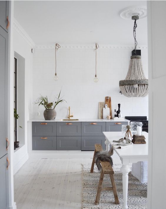 an eclectic kitchen with white walls and a whitewashed floor, grey cabinets, a statement bead chandelier over the dining space
