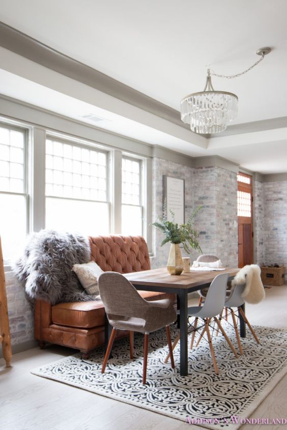 an elegant dining space in farmhouse style, with whitewashed brick walls, a crystal chandelier, a leather sofa and a printed rug