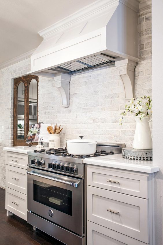 an elegant kitchen with whitewashed brick walls, vintage cabinetry, a large hood looks chic and cool
