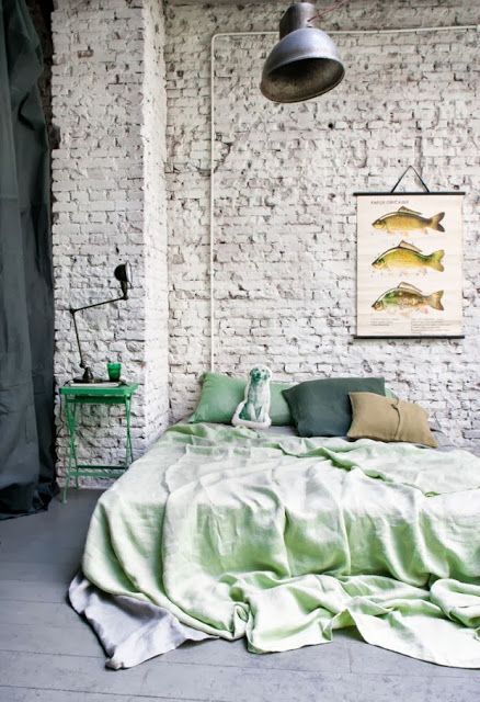 an industrial bedroom with a whitewashed brick wall, a bed with bright bedding, an industrial lamp and a catchy artwork