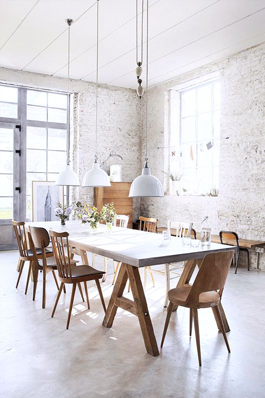 an industrial dining room with whitewashed brick walls, wooden and metal furniture, pendant lamps that highlight the height of the ceiling