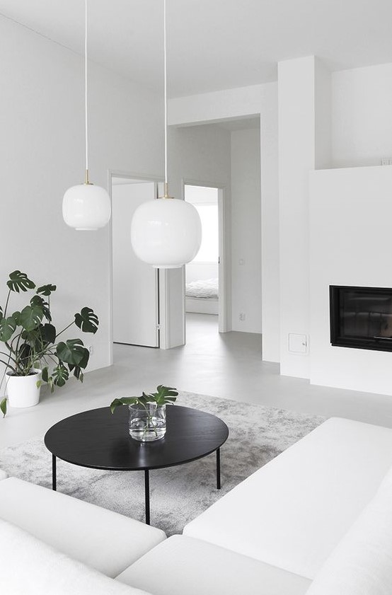 An ultra minimalist living room with a white sectional, a built in fireplace, a black table and white pendant lamps