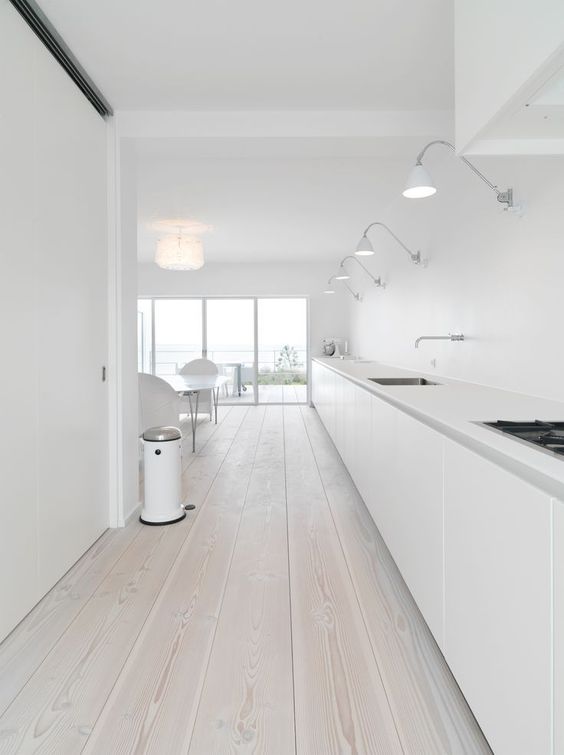 An ultra minimalist white kitchen with a whitewashed wooden floor that softens the look of the space a bit