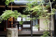 a Japanese courtyard with stone tiles, greenery, a stone bowl and a tree is a dreamy space that relaxes
