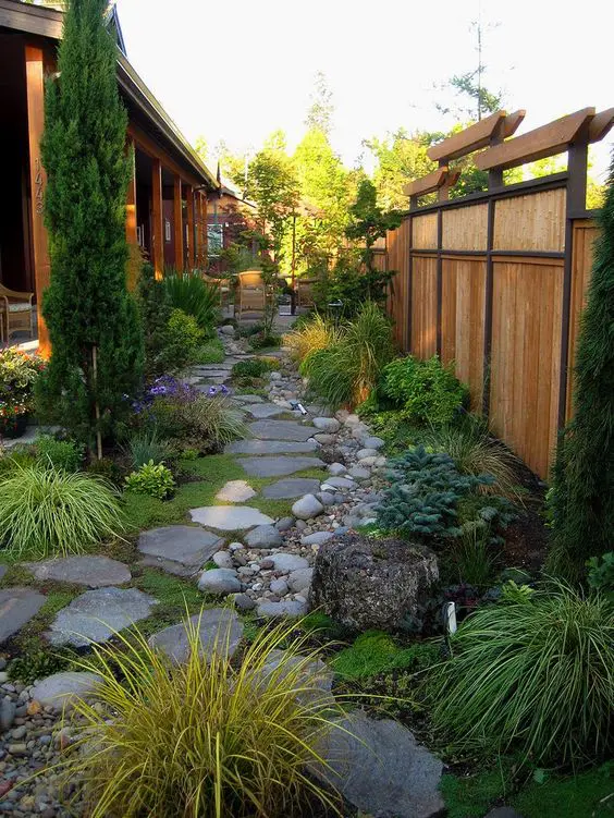 A Japanese inspired garden with rock tiles, pebbles, tree stumps, greenery, grasses and a tall tree for a zen look