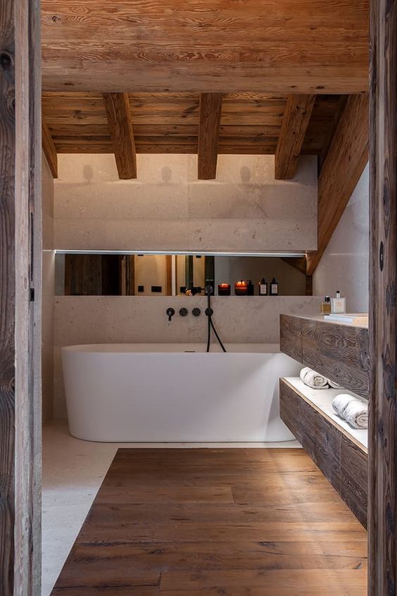 A beautiful chalet bathroom clad with white stone and rich stained wood, with a floating vanity and a large bathtub is amazing
