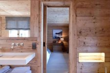 a blonde wood chalet bathroom with a floating sink and vanity, a bathtub clad with stone and a lit up niche