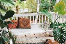 a boho front porch with a rug, a hammock, lots of lanterns hanging, potted plants and candles around