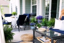 a bold boho summer porch with navy furniture, a printed rug, jute ottomans, a glass coffee table and lots of potted greenery