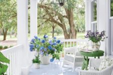 a bright summer porch done in white with touches of juicy green, blooms, lanterns and wicker furniture