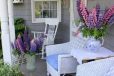 a bright summer porch with white furniture and super colorful blooms in pots and urns