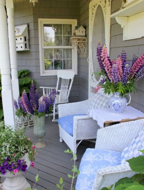 a bright summer porch with white furniture and super colorful blooms in pots and urns