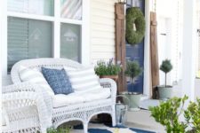 a bright summer porch with white wicker furniture, potted greenery and blooms and a printed rug