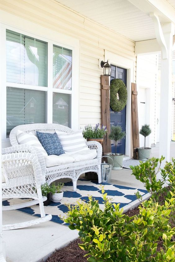 a bright summer porch with white wicker furniture, potted greenery and blooms and a printed rug