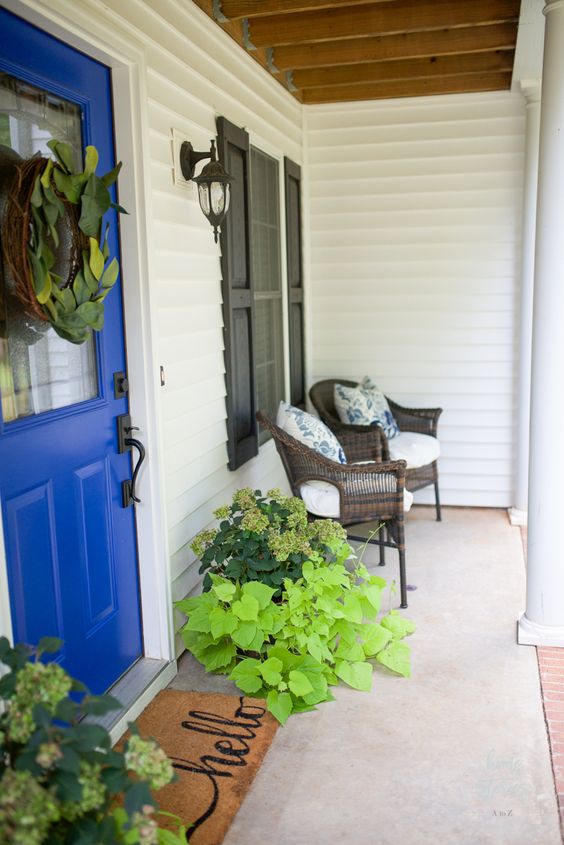 a bright summer porch with wicker furniture, shutters, a rug, potted greenery and floral pillows