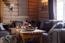 a chalet living room with wooden walls and a ceiling, grey sofas, a boho hanging on the wall and a wooden table
