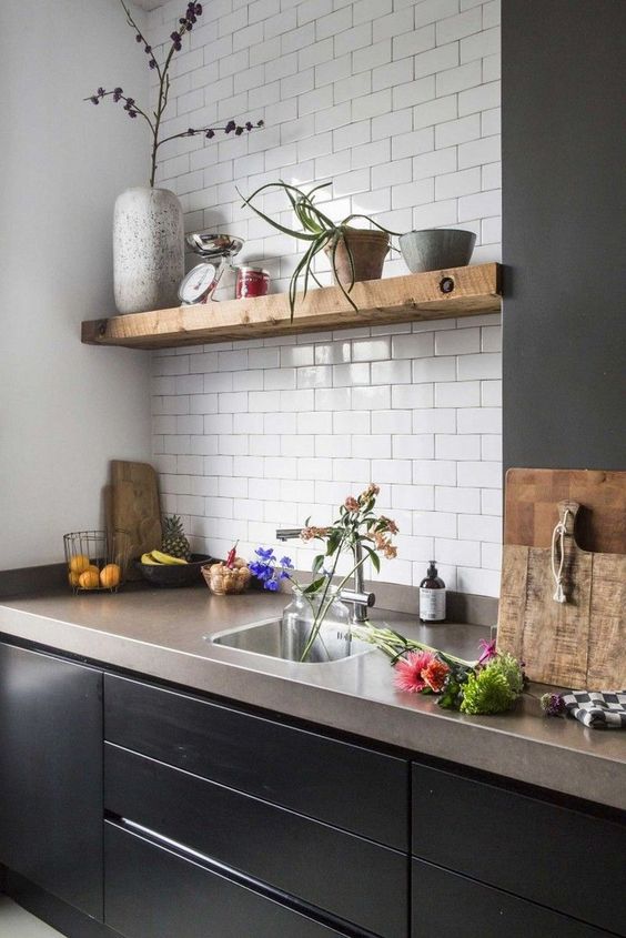 a chic kitchen with sleek black cabinets, open shelves, a white subway tile backsplash and concrete countertops
