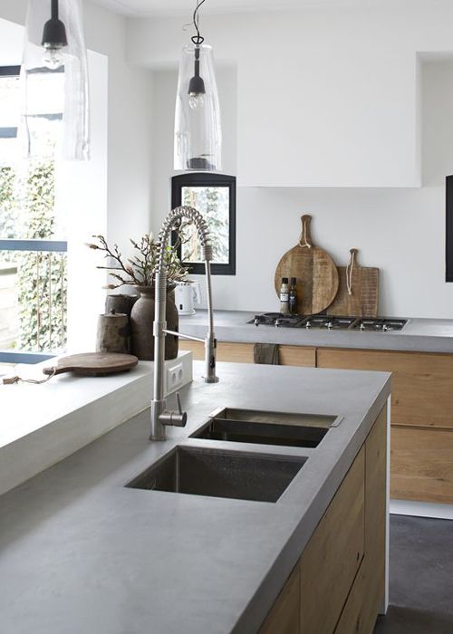 a chic minimalist kitchen with sleek wooden cabinets, concrete countertops, white walls and pendant lamps