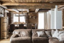 a chic modern chalet living room with a stained wooden ceiling and beams, a leather sofa, a gorgeous wood slcie table
