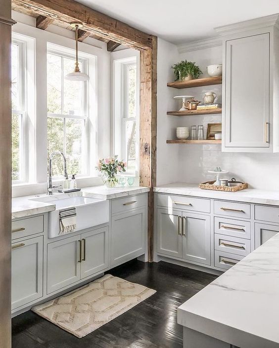 a chic off-white kitchen with neutral stone countertops, gold hardware and rough wooden beams