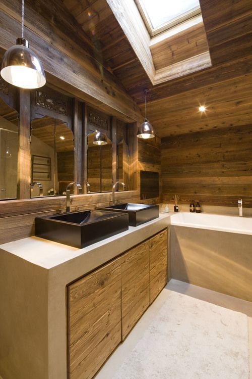 a contemporary chalet bathroom clad with natural wood, with neutral sone, a bathtub and two black sinks, a skylight and pendant lamps