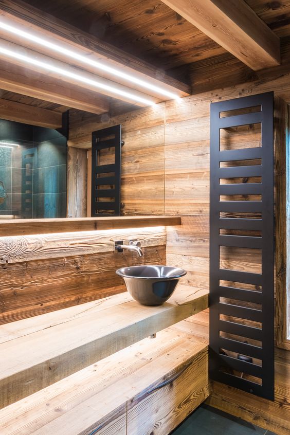 a contemporary chalet bathroom clad with wood, with a lit up shelf vanity, a black bowl sink and a modern radiator