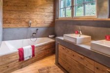 a contemporary chalet bathroom clad with wood, with wooden beams on the ceiling, a large vanity with a concrete countertops and a geometric tub