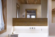 a contemporary chalet bathroom with wood, a tub clad with wood, white appliances and a large mirror plus a built-in vanity