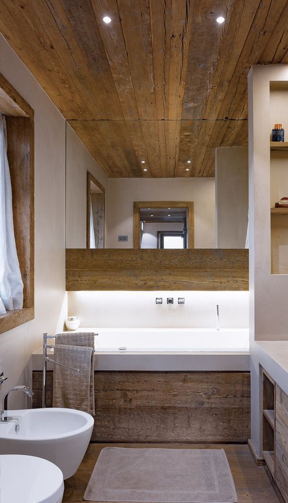 A contemporary chalet bathroom with wood, a tub clad with wood, white appliances and a large mirror plus a built in vanity