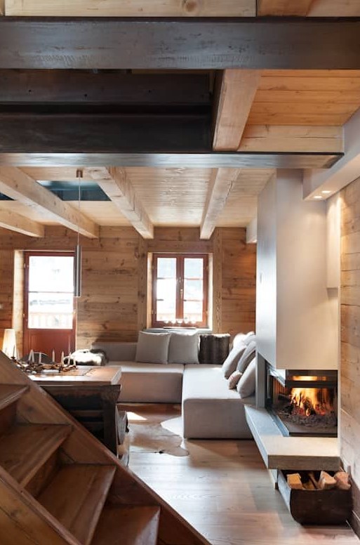 a contemporary chalet living room clad with wood, with a modern fireplace and some firewood stored